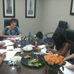 Five women are sitting at a conference table, taking notes, with snacks and drinks spread around.