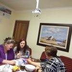 Three women seated around a table in a meeting room, discussing paperwork with pens and notes on the table. A painting hangs on the wall.