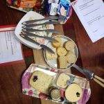 A table set with cheese, crackers, fruits, vegetables, yogurt, multiple knives, and papers titled "Communicating with assertiveness and confidence.