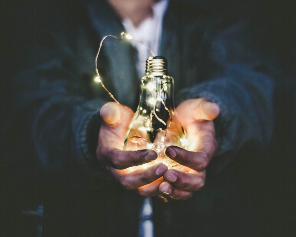 Hands holding a glowing light bulb, symbolising ideas and insights in coaching.