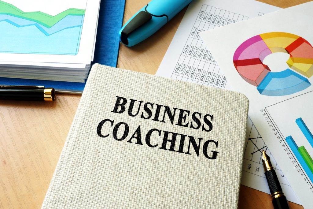 Notebook labeled "Business Coaching" on a desk with charts, graphs, a pen, and a highlighter.