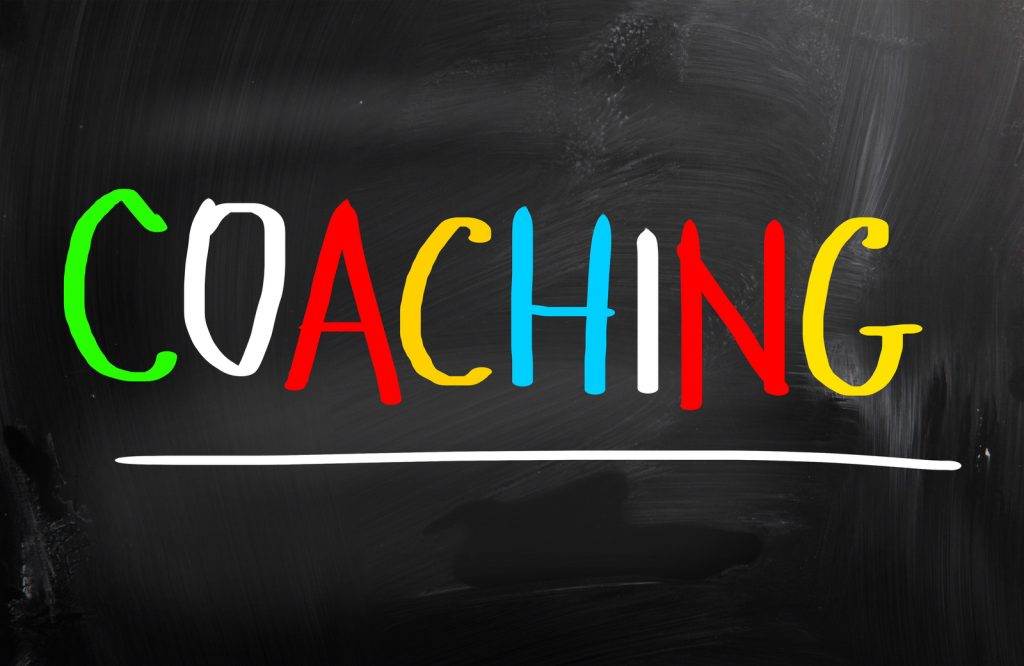 The word "coaching" is written in colorful letters on a black chalkboard background with a white underline.