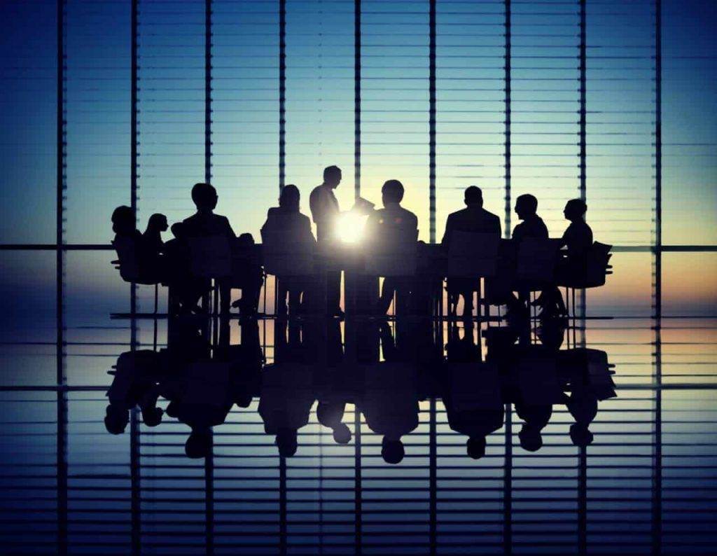 Silhouetted business team in a meeting room at sunrise, exemplifying team coaching to transform your team dynamics.