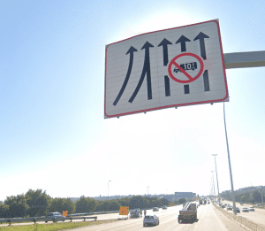 Highway sign indicating four lanes with arrows; heavy vehicles over 10 tons are prohibited from entering the second lane from the right.
