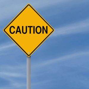 Yellow caution sign on a pole against a blue sky background with wispy clouds.