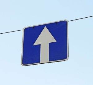 Blue road sign with a white upward arrow, indicating one-way traffic.