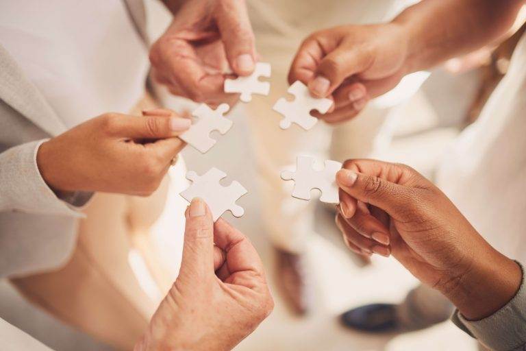 Hands of diverse people holding puzzle pieces, symbolizing teamwork and collaboration.