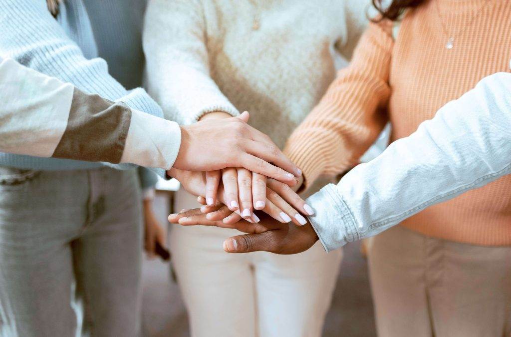 Close-up of diverse team members stacking hands in a gesture of unity, demonstrating the stages of team development.
