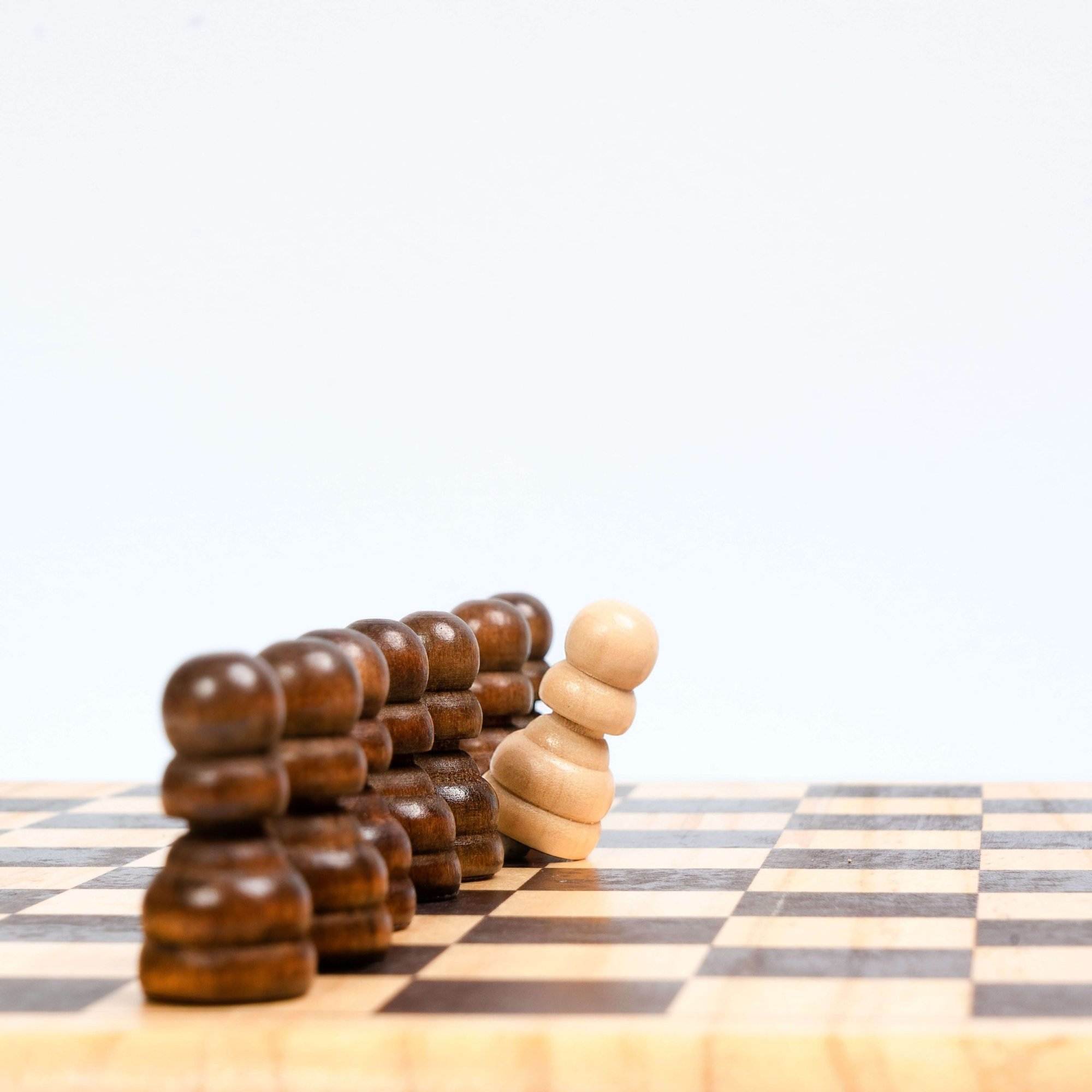 Chess pieces on a board, with a single white pawn in front of a row of brown pawns, appearing to tilt forward.