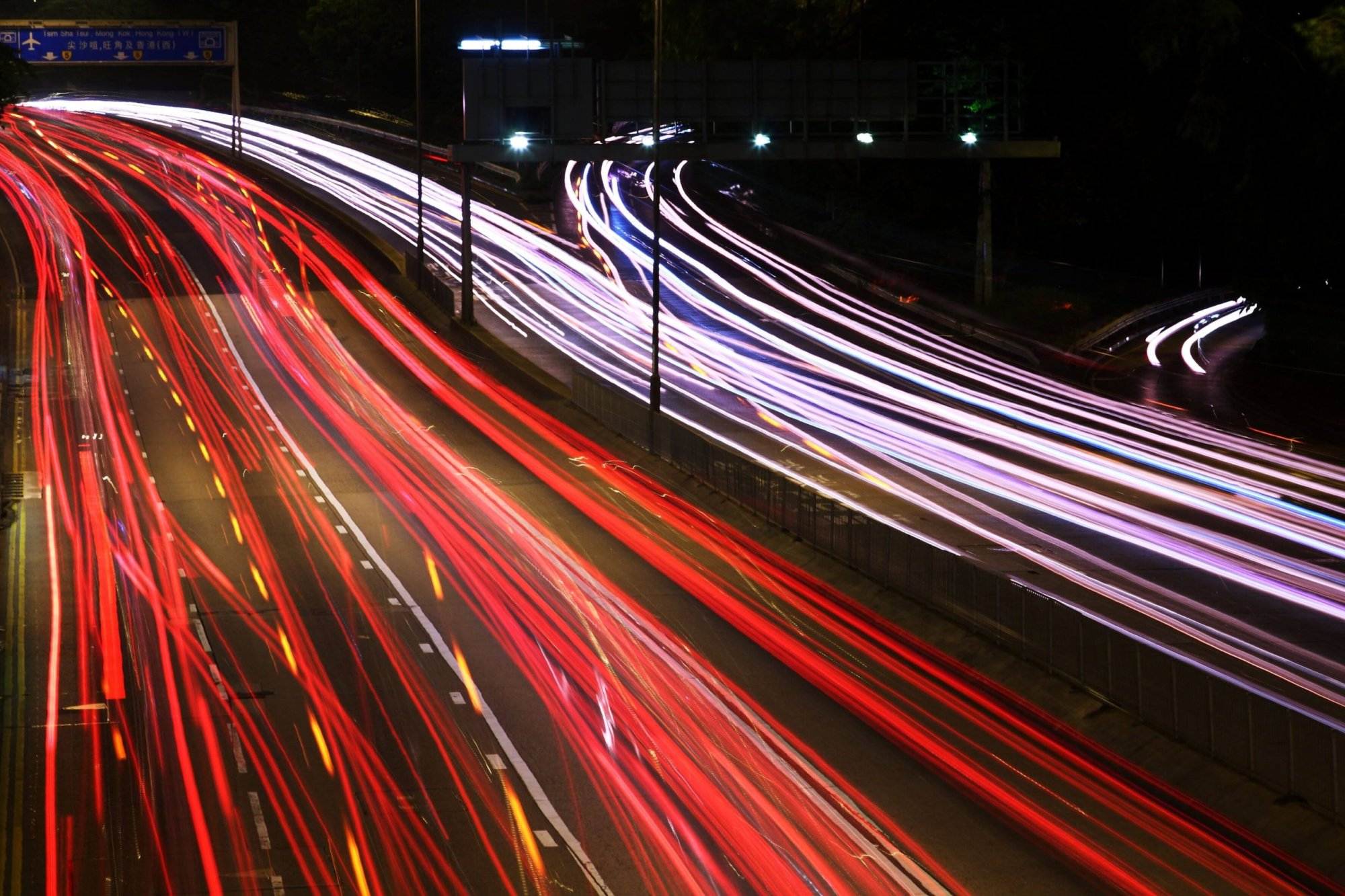 Long-exposure photograph of a highway at night, capturing red and white light trails from moving vehicles.