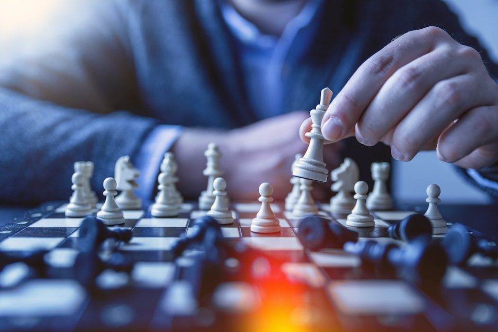 Close-up of a person in a suit moving a chess piece on a board, symbolizing strategic thinking in business development coaching.
