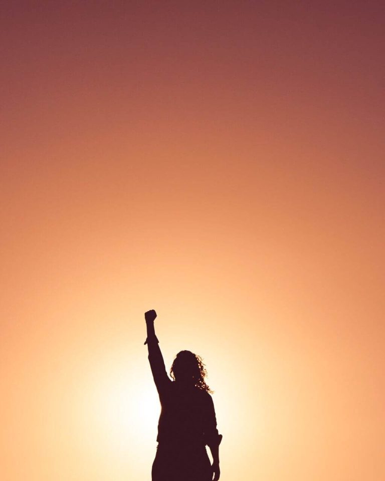 Silhouette of a person with a raised fist against a warm, glowing sunset sky.