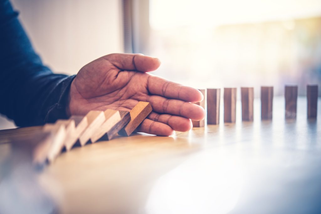 A hand stops falling dominoes, symbolizing cultural values of intervention and prevention.
