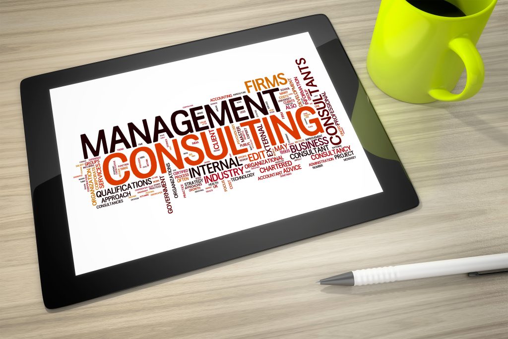 Tablet displaying a word cloud focused on "Management Consulting," on a desk with a yellow mug and a pen.