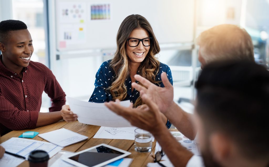 Team members engaging in a collaborative meeting, discussing documents and smiling, illustrating team development dynamics.