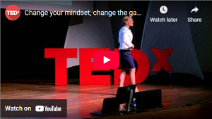 Speaker in white shirt on stage with TEDx sign, giving a talk titled "Change your mindset, change the game" on YouTube.