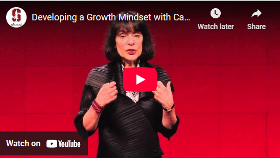 Woman speaking on stage about growth mindset, with a YouTube play button overlay. Background is red.