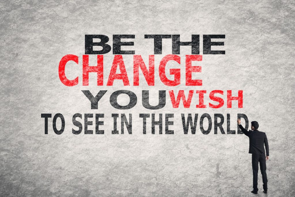 Man writing "Be the change you wish to see in the world" on a textured wall.