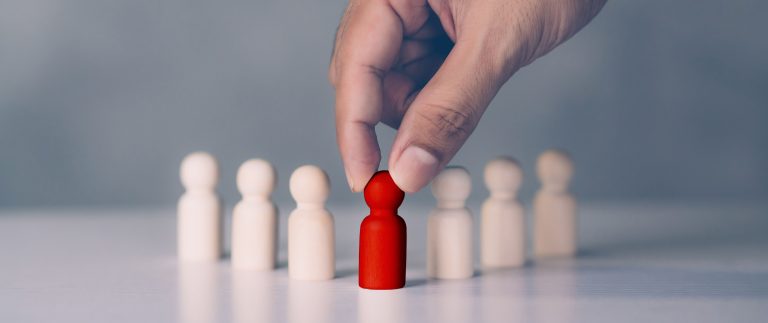 Hand selecting a red figurine among white ones, symbolizing succession planning and leadership selection.