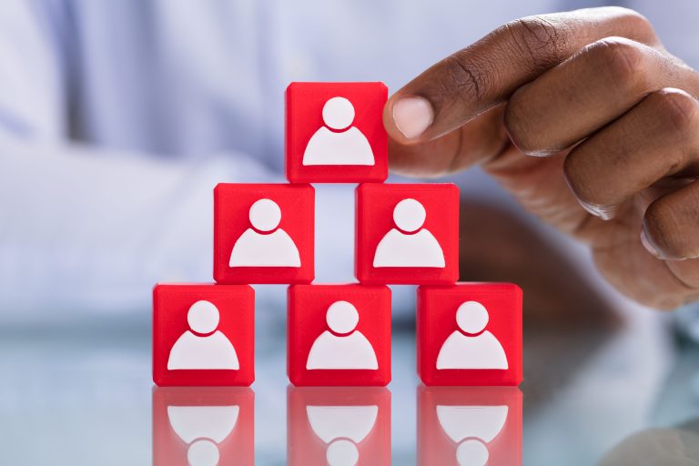 Hand stacking red blocks with person icons, illustrating succession planning concept.
