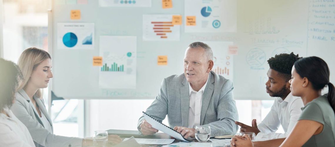 A group discussion during an executive coaching session with charts and data on a whiteboard in the background.