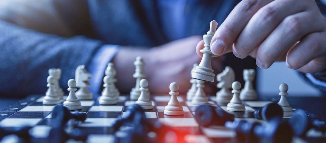 Close-up of a person in a suit moving a chess piece on a board, symbolizing strategic thinking in business development coaching.