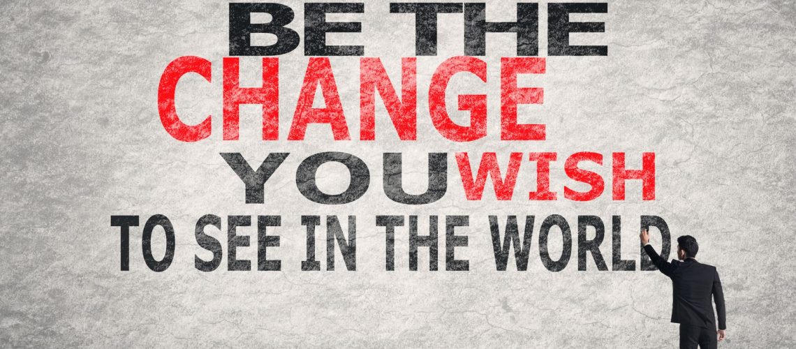 Man writing "Be the change you wish to see in the world" on a textured wall.