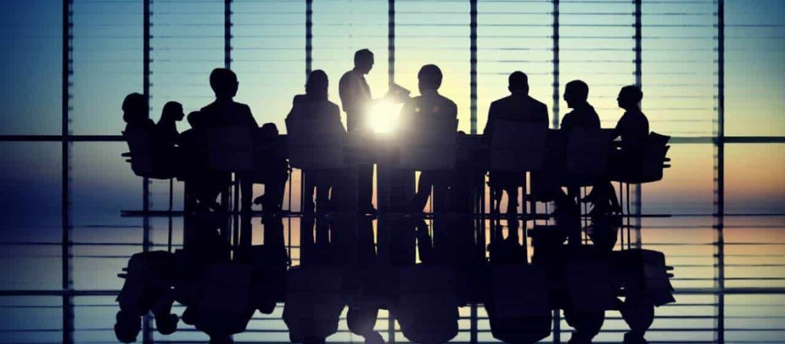 Silhouetted business team in a meeting room at sunrise, exemplifying team coaching to transform your team dynamics.