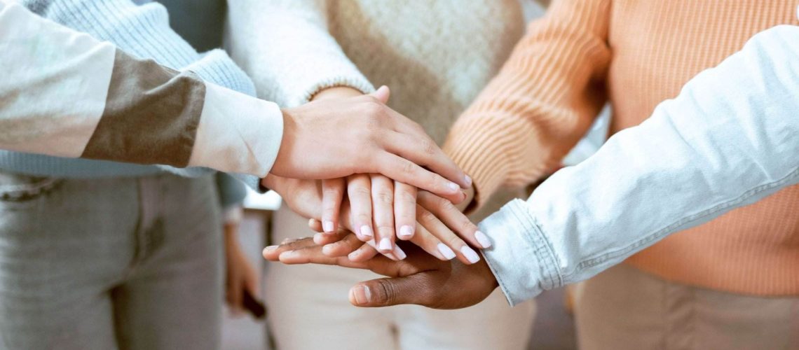 Close-up of diverse team members stacking hands in a gesture of unity, demonstrating the stages of team development.