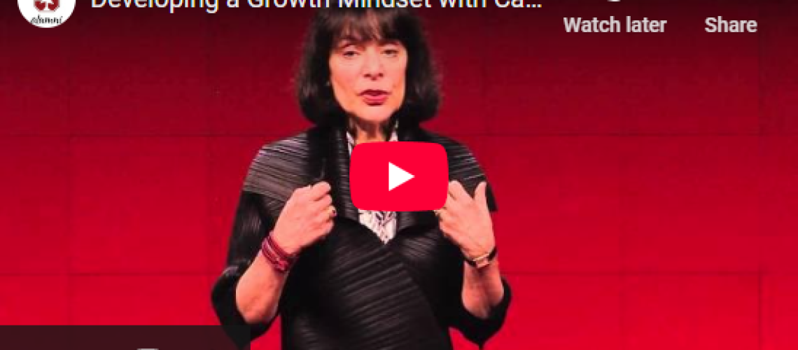 Woman speaking on stage about growth mindset, with a YouTube play button overlay. Background is red.