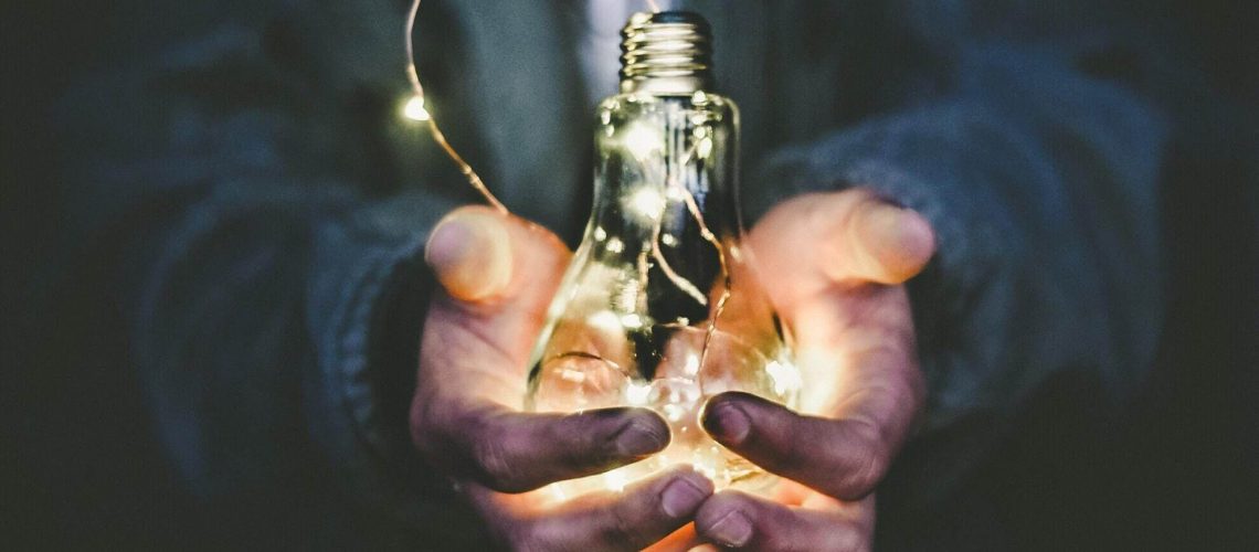 Hands holding a glowing light bulb, symbolising ideas and insights in coaching.